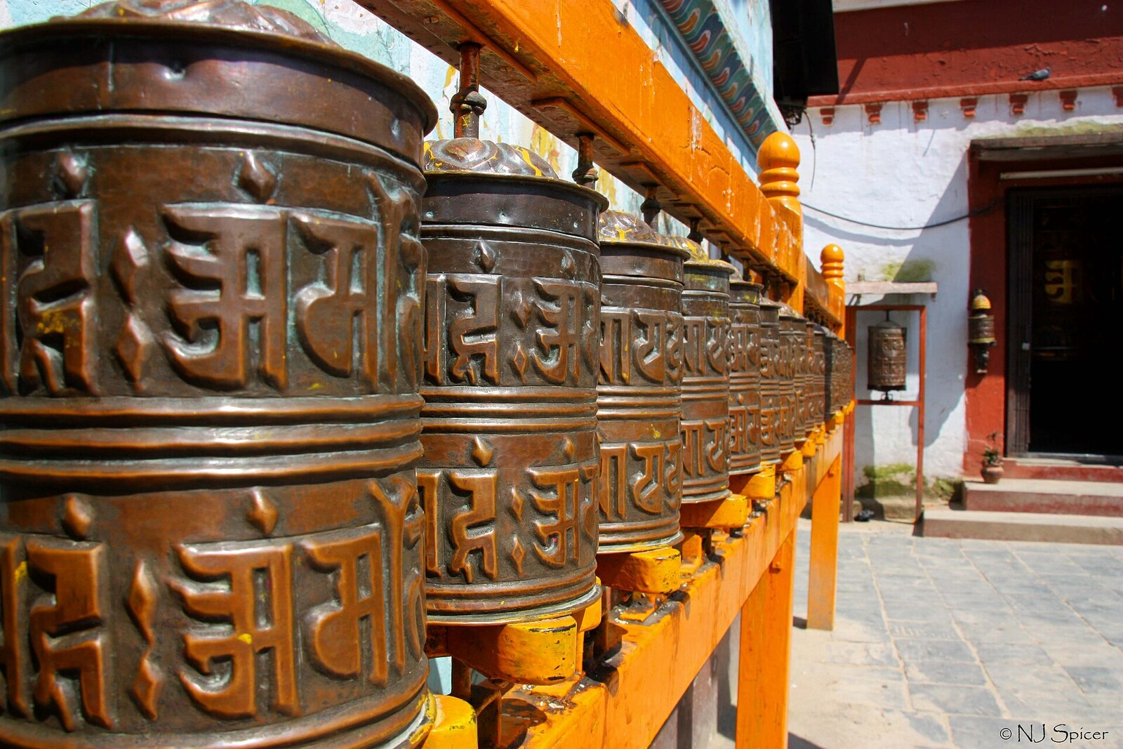 A row of copper prayer wheels against the stupa wall