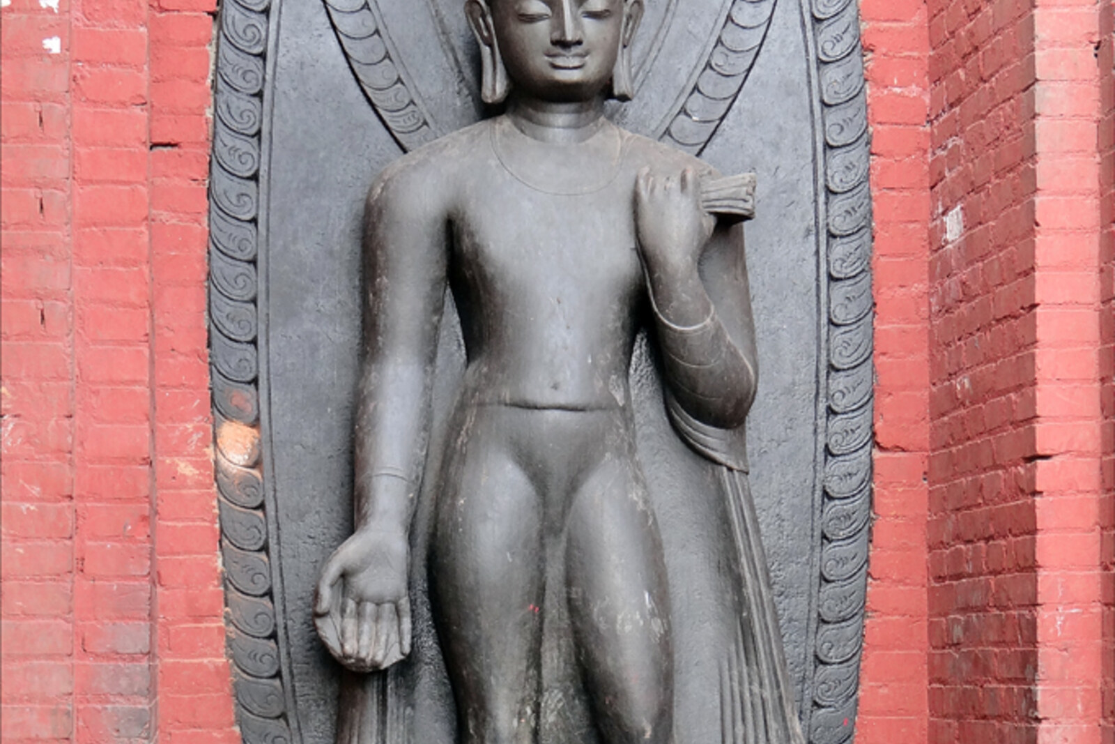 A black stone statue of Dipankara Buddha in a blessing gesture, surrounded by small stupas.