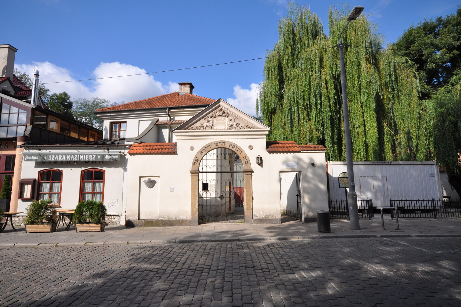 A small white synagogue with a triangular gable and a green courtyard