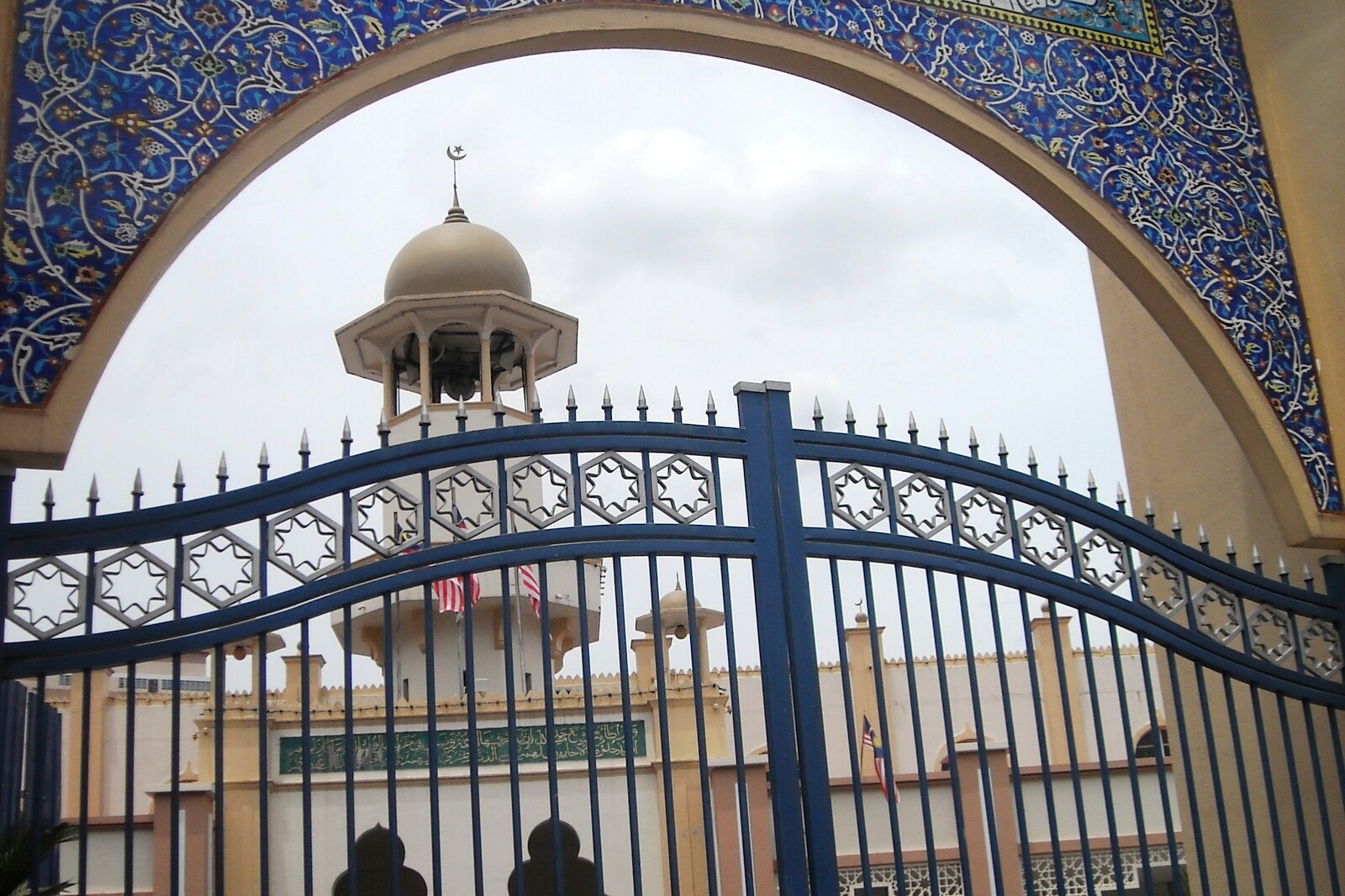 A white mosque with a brown roof and a minaret among trees.