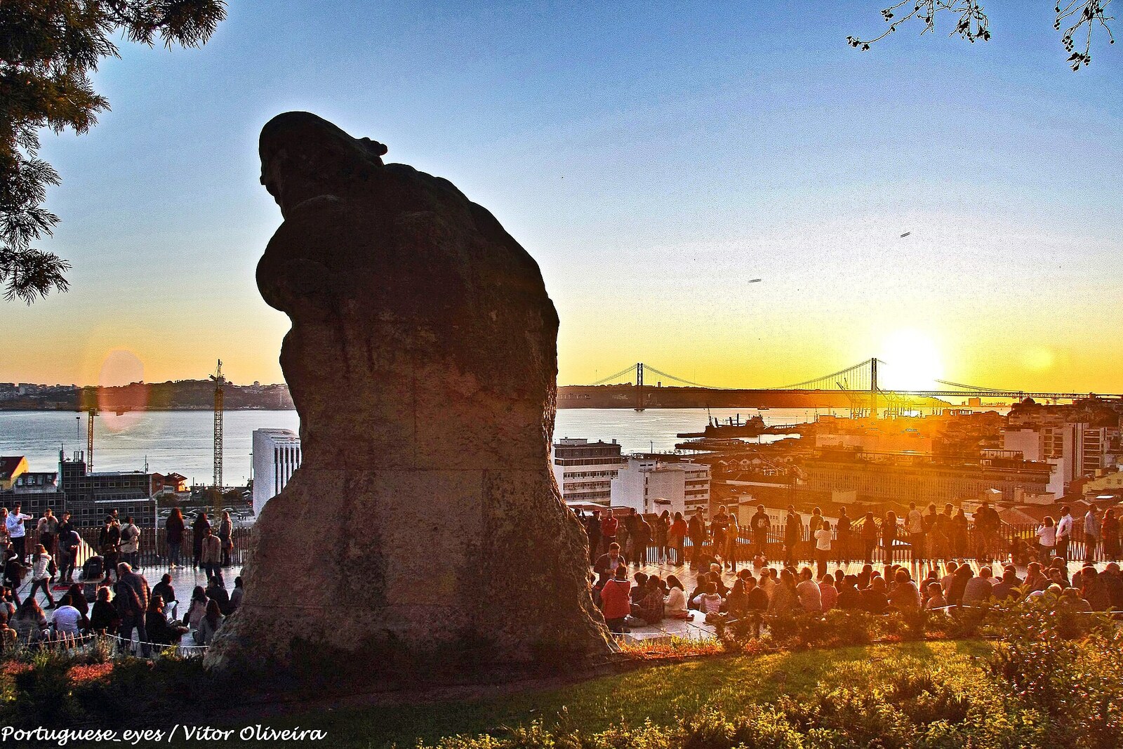 The Miradouro de Santa Catarina terrace, with a white statue of Adamastor and a view of the bridge across the river.