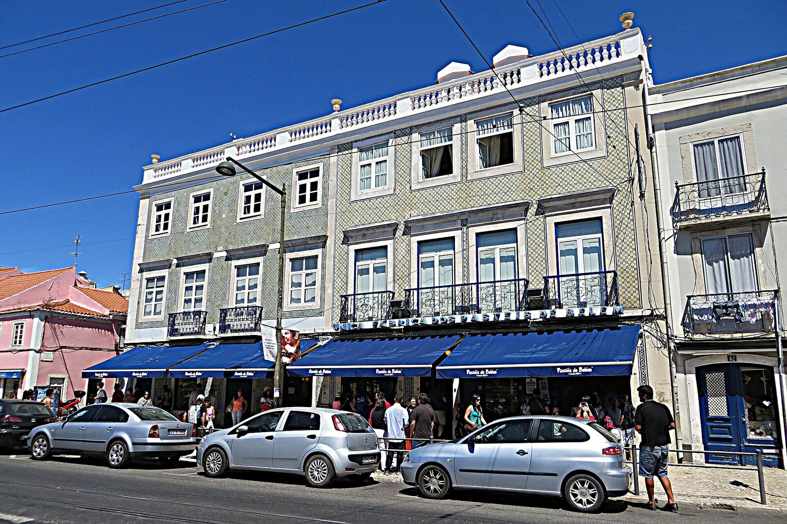 Facade of the Pastéis de Belém pastry shop with blue signs and people at the entrance