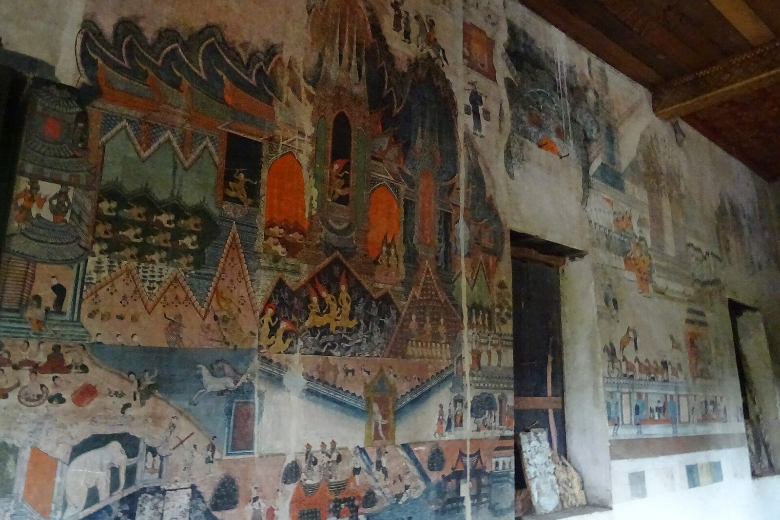 Fading wall murals at Wat Pa Huak, with palaces, processions, and small figures.