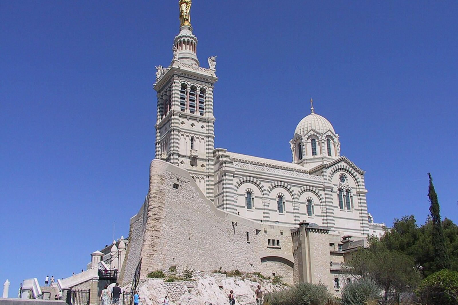 A light-colored church with a golden statue rises on a hilltop above the cityscape.