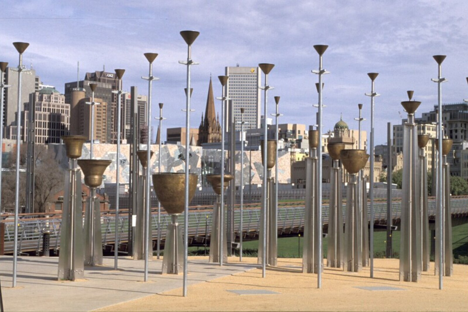 A row of bronze bells of different sizes in an open area of a park