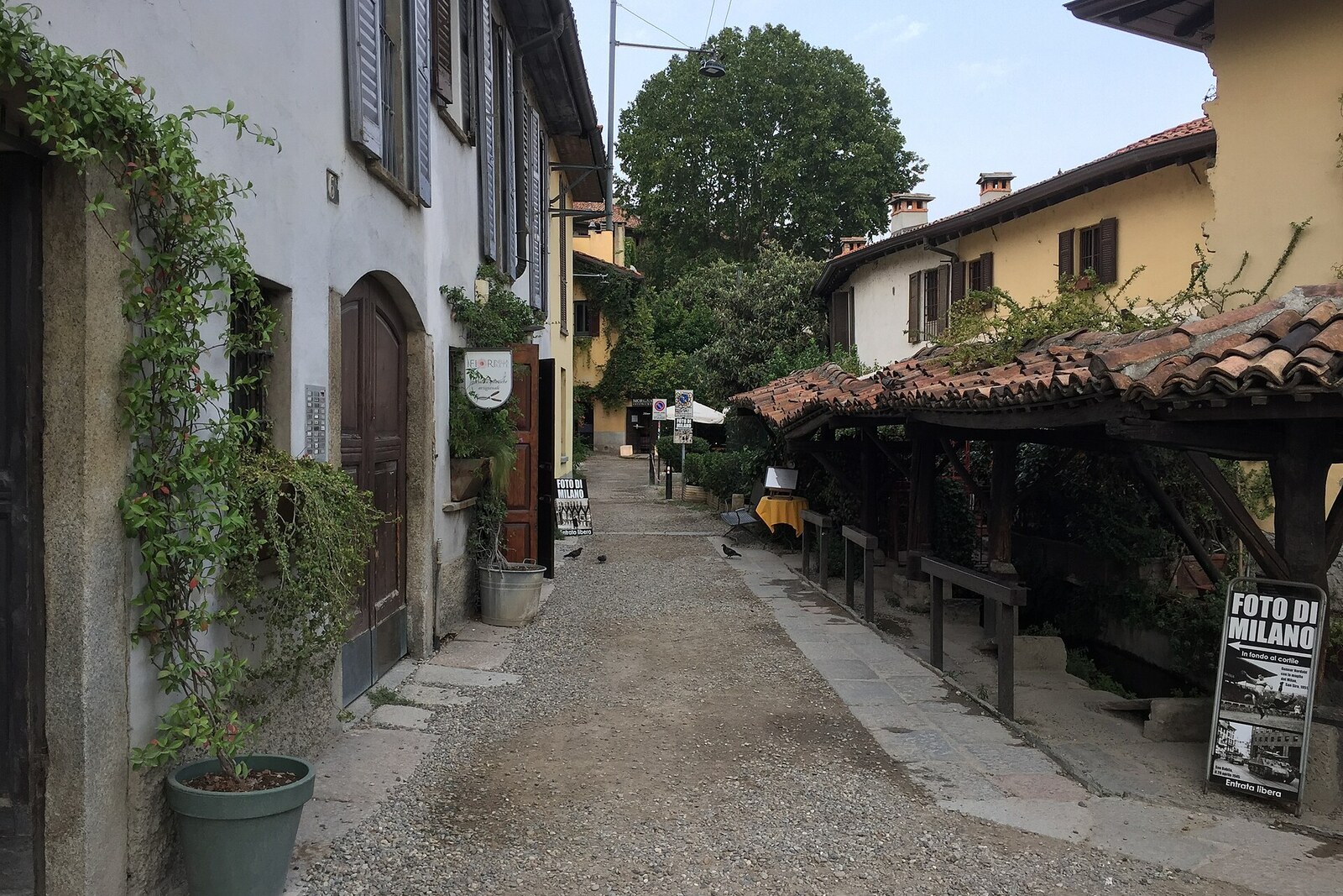 A quiet laundry alley in Milan with stone slabs, wooden boards, and a narrow stream