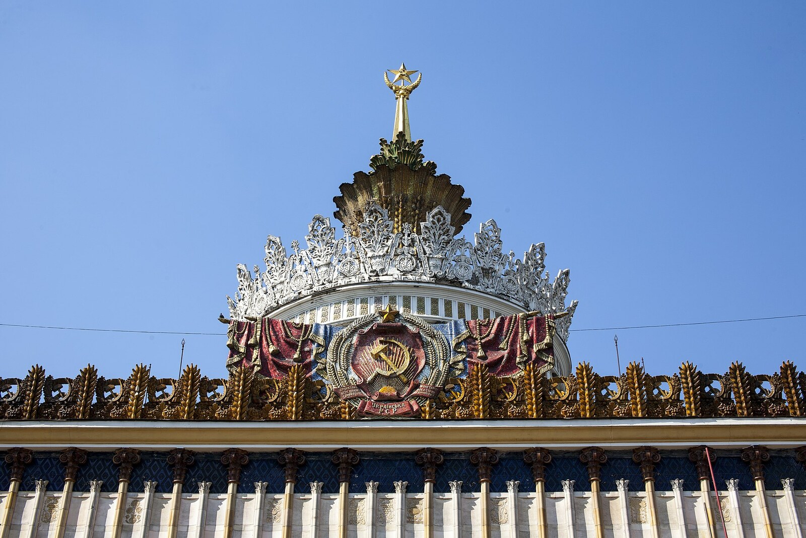 The coat of arms of the Ukrainian SSR, ears of grain, and a decorative crown on the facade of Pavilion No. 58.