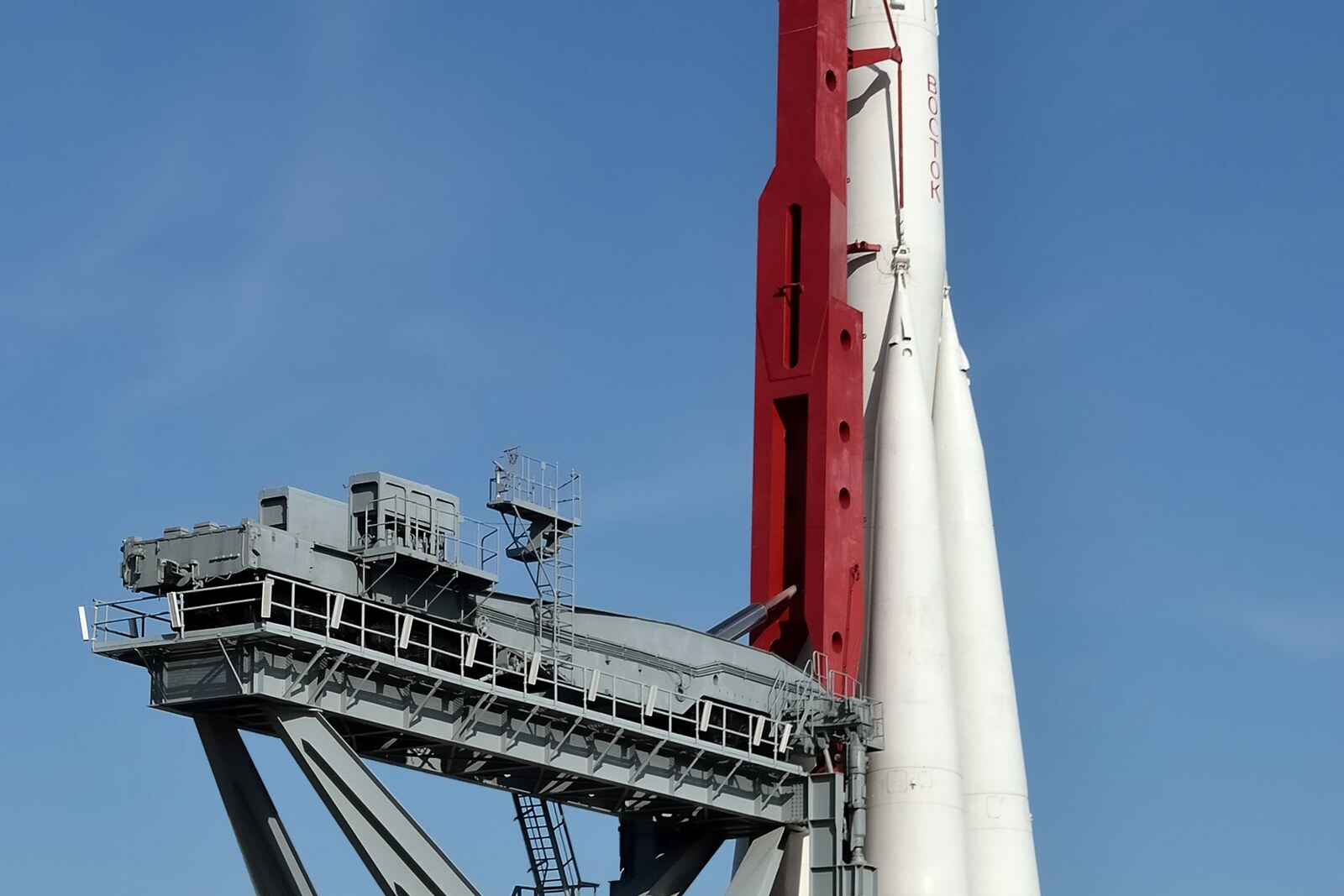 The white Vostok launch vehicle in an upright position beside a red and gray service gantry.