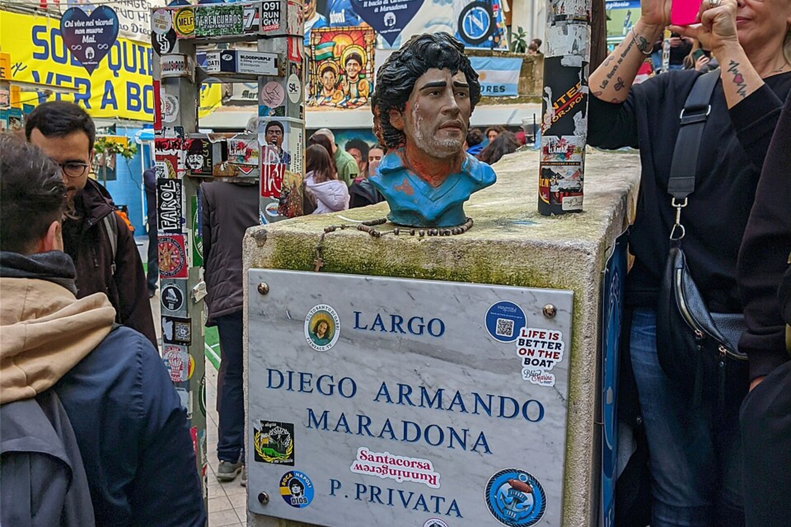 An altar at Largo Maradona with a portrait of Diego Armando Maradona, flags, and candles