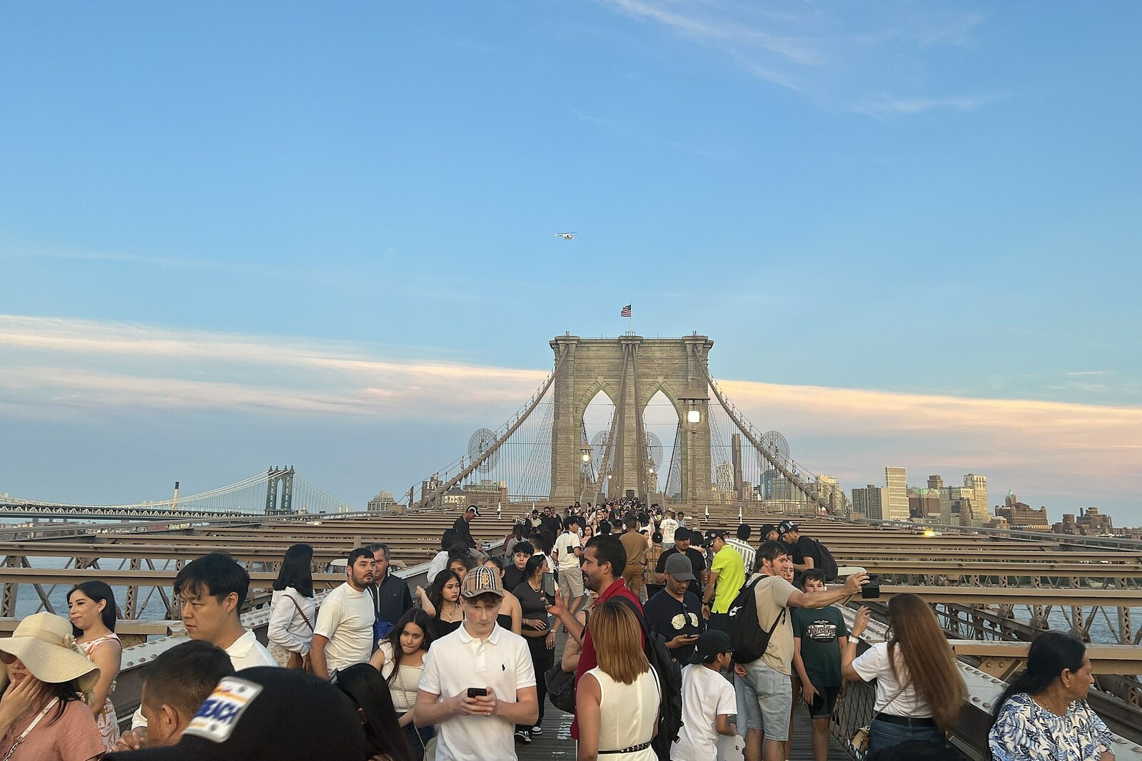 People walk along the wooden path of the Brooklyn Bridge, surrounded by taut steel cables