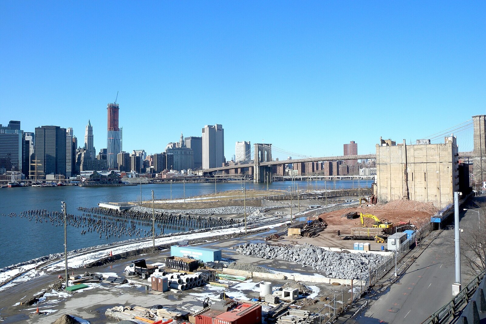 Des gens se promènent sur les pelouses vertes de Pier 1 ; derrière eux se trouvent les gratte-ciel de la ville et le fleuve