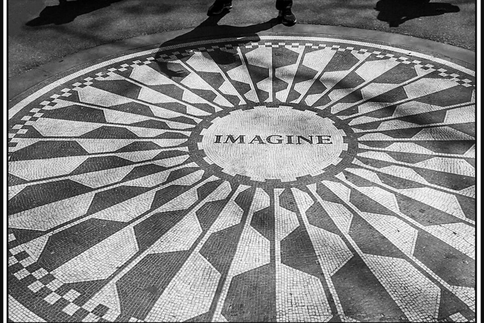 A round mosaic of gray and white stones bearing the word “Imagine,” surrounded by greenery