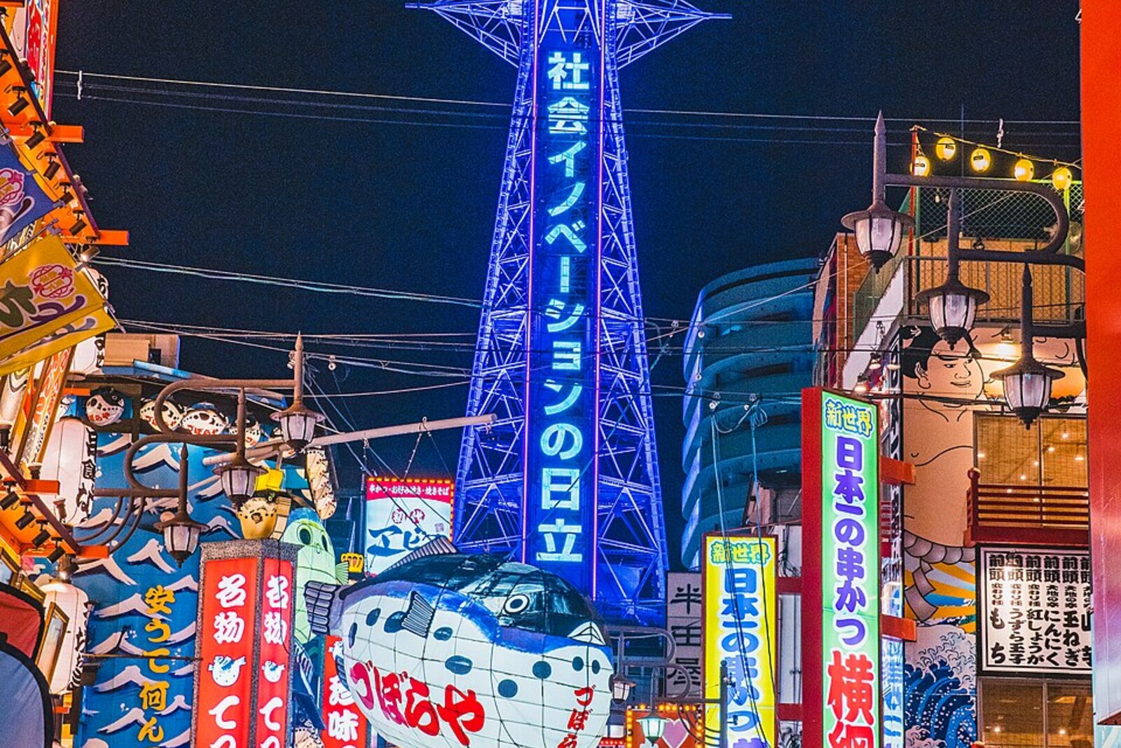 Foto nocturna de la Torre Tsutenkaku y de una calle de Shinsekai con luces de neón.