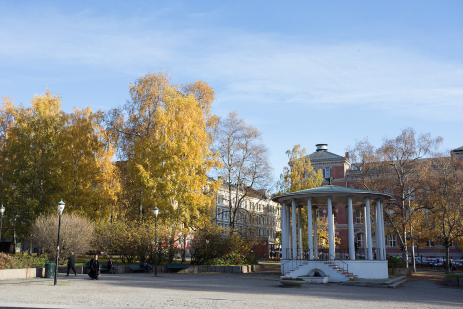 An autumn view of Birkelunden Park with yellow trees, a bandstand, and houses in Grünerløkka.
