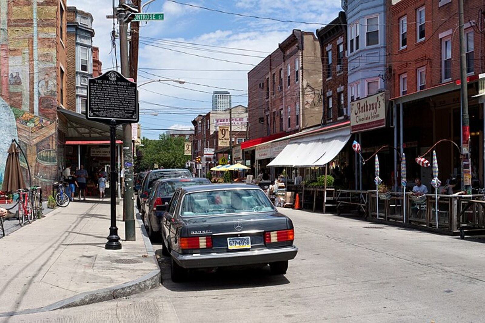 Panoramic view of the South 9th Street Italian Market in Philadelphia, with a long row of shops under bright striped awnings and a wide street.