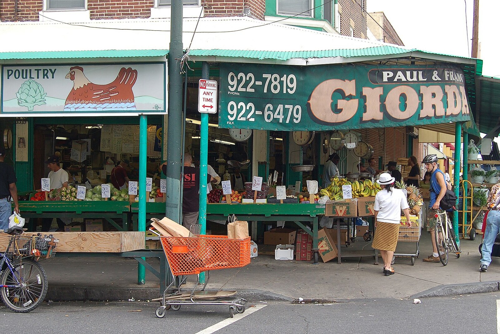 A merchant at the Italian Market stands behind a counter with peppers, tomatoes, and other vegetables.