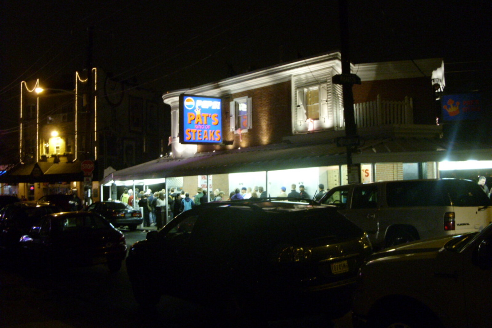 Pat's corner establishment with a neon sign and a line of customers.