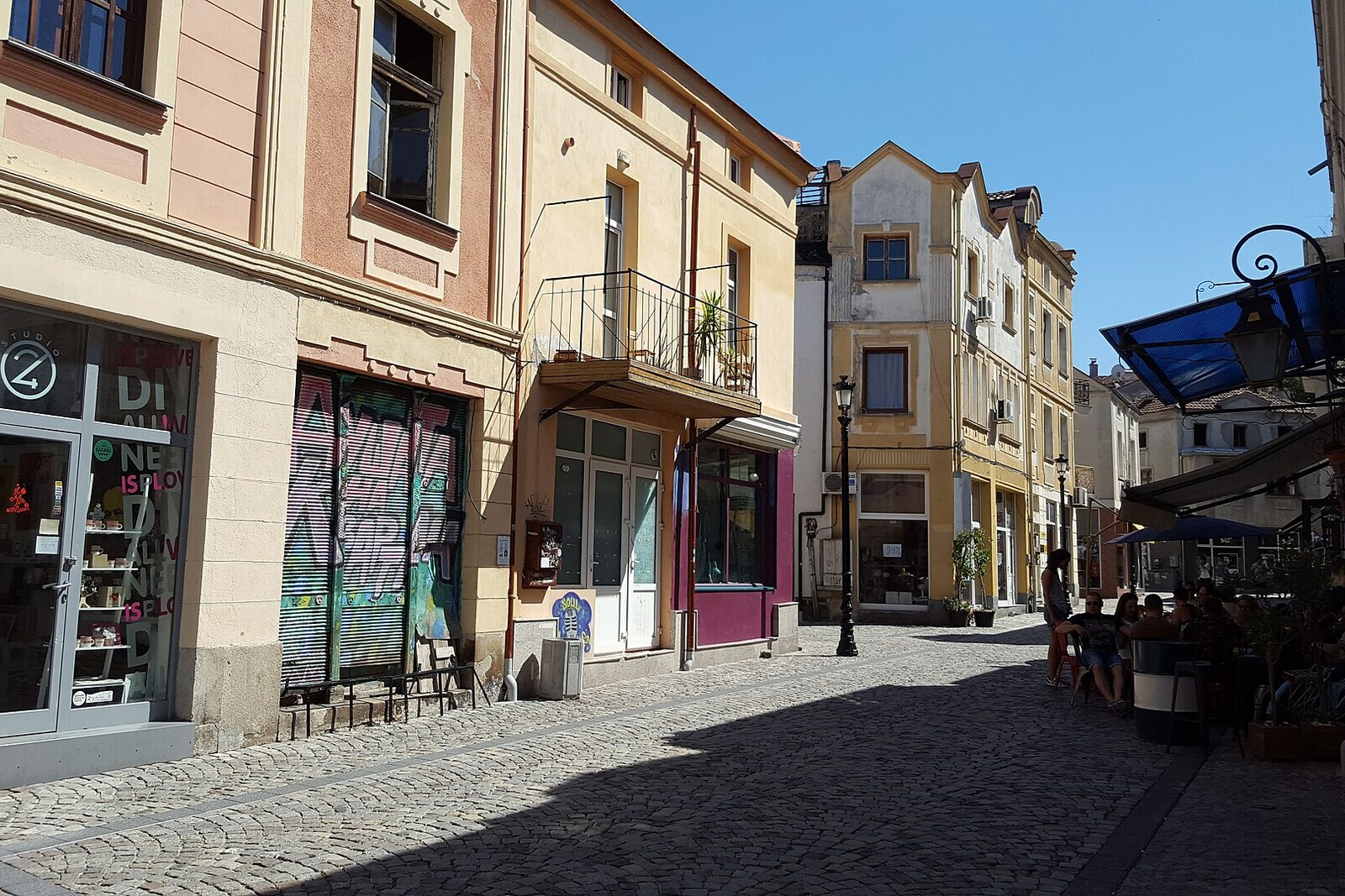 Narrow cobbled Zlatarska Street in Kapana with workshops, murals, and tables