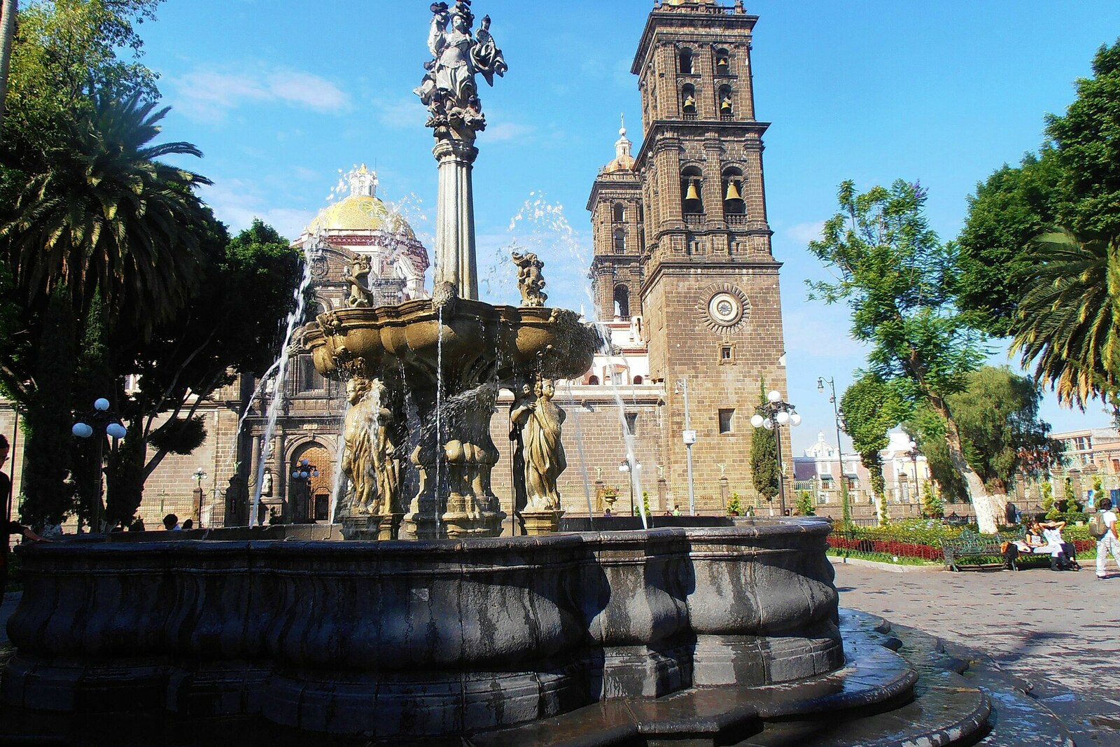 La Fuente de San Miguel en el Zócalo de Puebla; tras los árboles se ve una torre de la catedral.