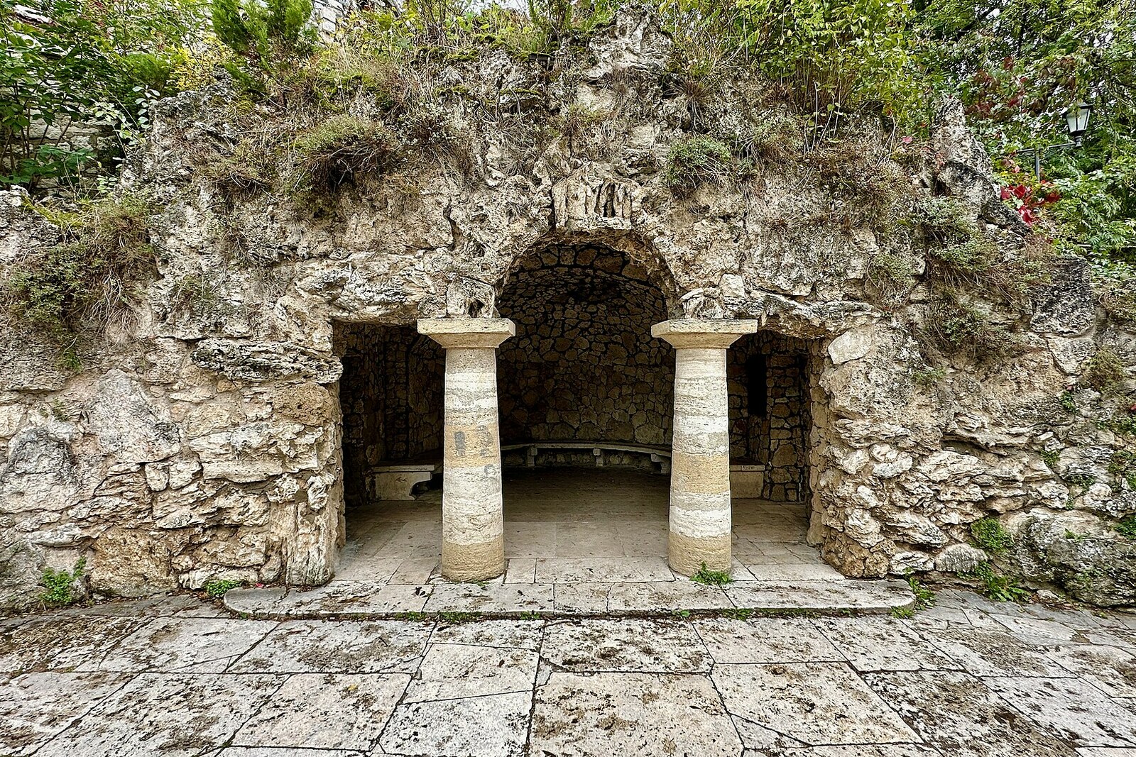 The stone arch of the Grotto of Diana, with two light-colored columns and a bench inside.