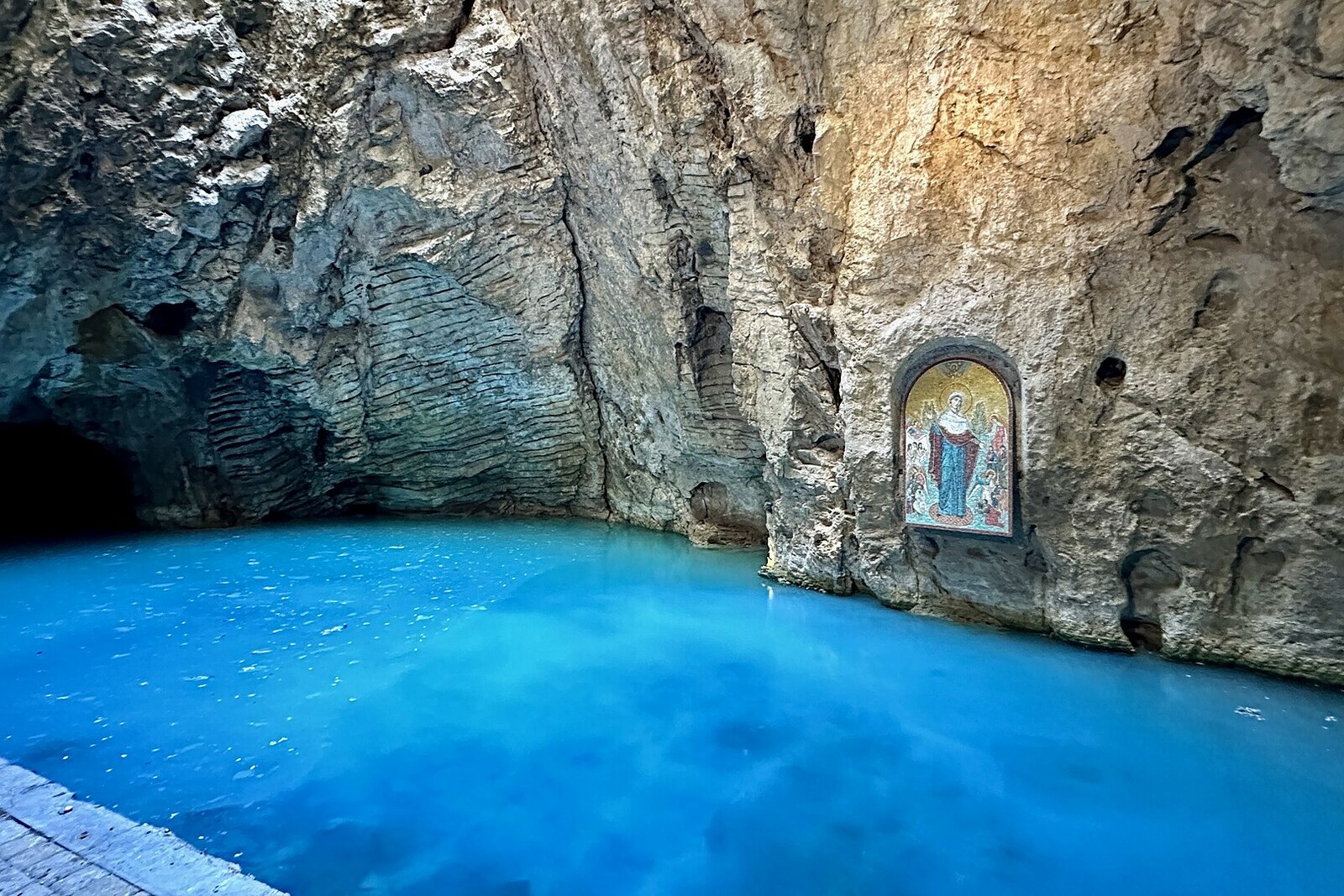 Turquoise water of Lake Proval in a stone cave, with an image on the wall above it.