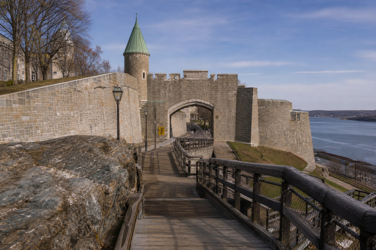 Stylized view of Québec City’s stone walls running along a cliff toward the river, with no people.