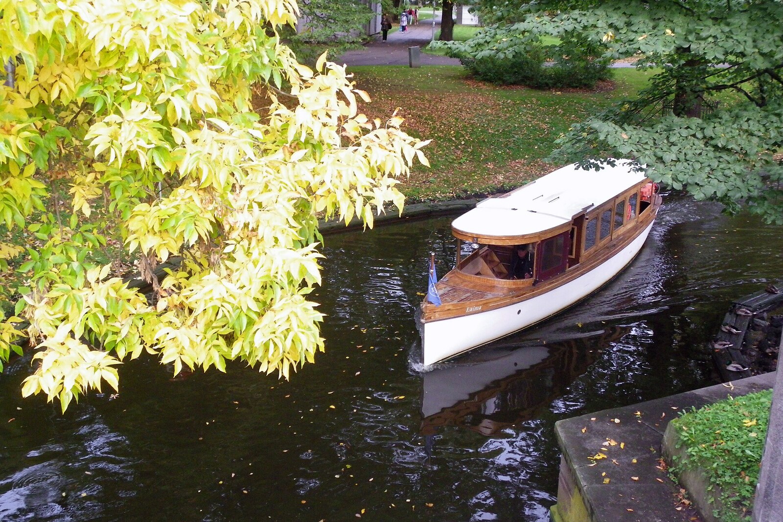 A boat on the Riga Canal in Kronvalda Park, among green banks and trees.