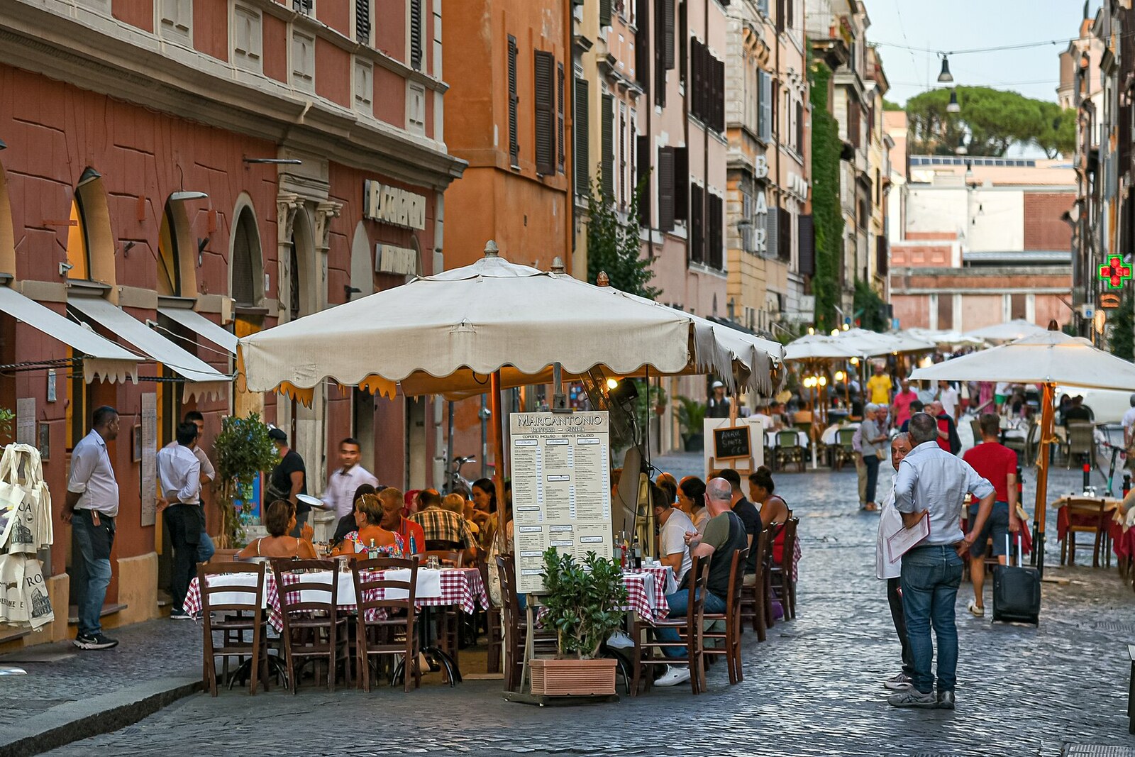 A sunny day on Borgo Pio, with restaurants, tables, and signs.