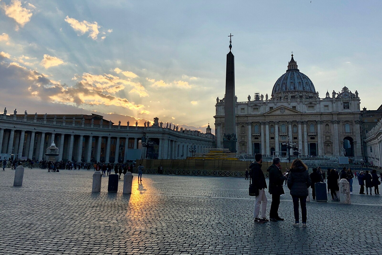 Panoramic view of St Peter's Square with the obelisk, fountains, and people.