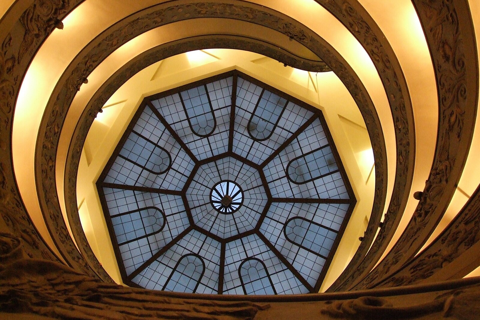 Spiral staircase in the Vatican Museums, looking upward toward a glass dome.