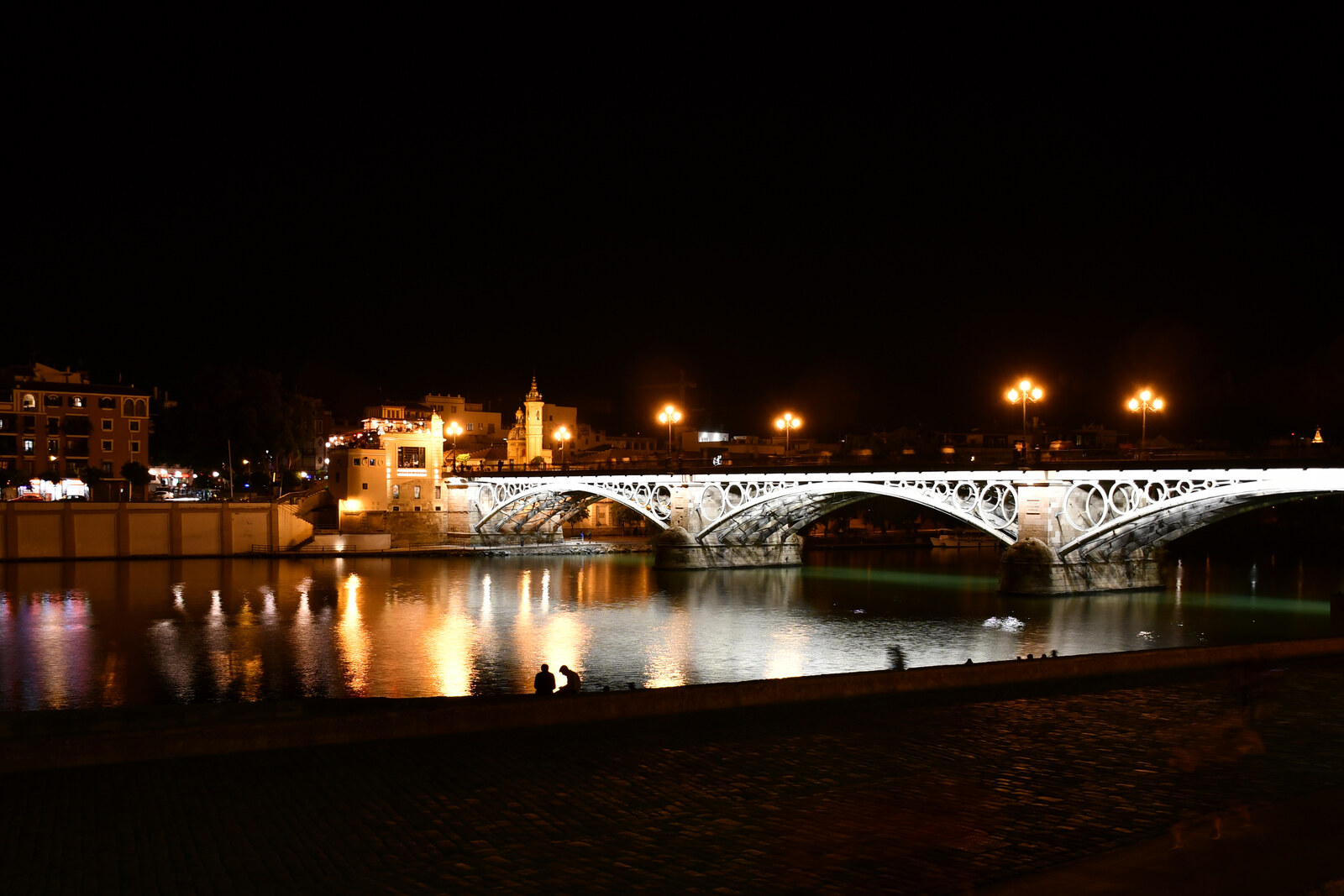 Night view of Triana Bridge across the Guadalquivir River and the Chapel of Carmen in the Triana district of Seville.