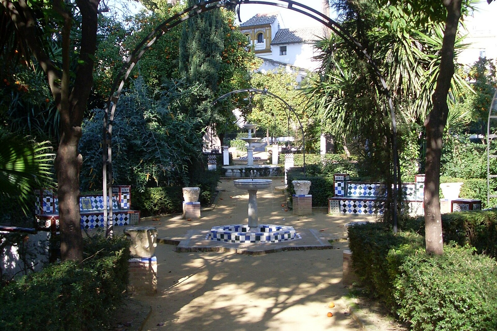 A green path in Murillo Gardens with colorful benches and orange bushes.