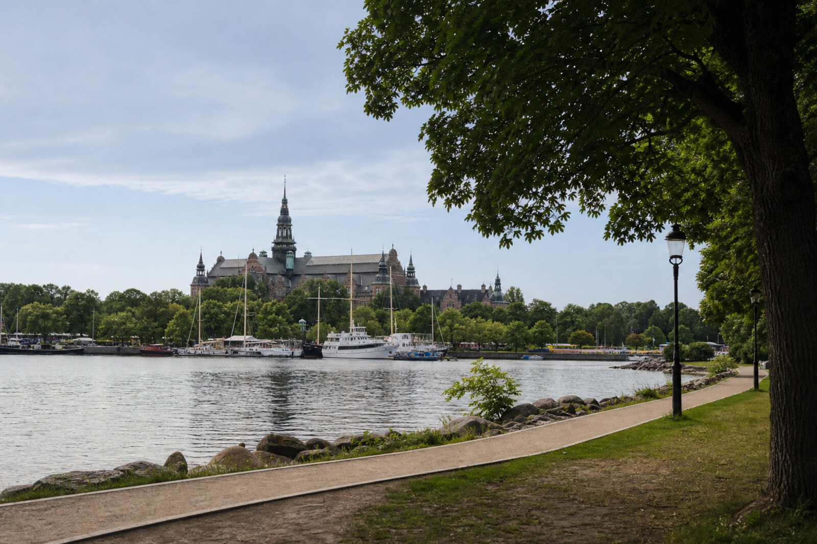 Panoramic view of Djurgården: a green island, the silhouette of Vasa, and museum spires against the water and evening sky