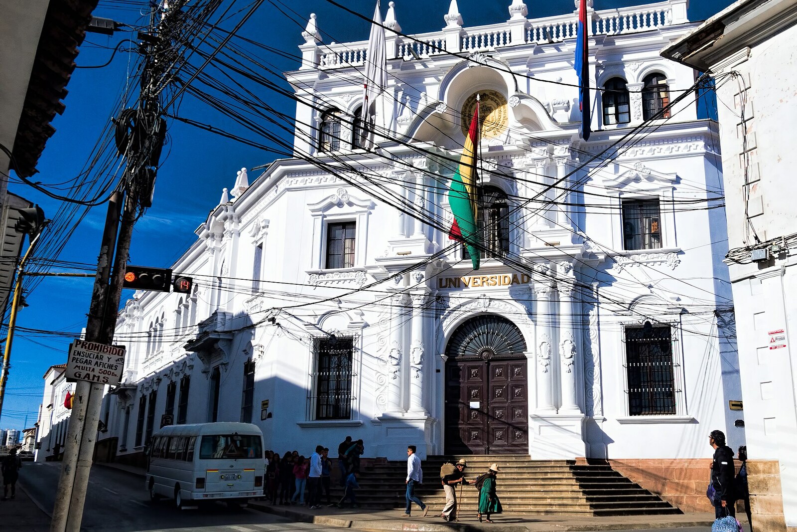 Façade blanche de l’Universidad Mayor, Real y Pontificia de San Francisco Xavier de Chuquisaca, avec des drapeaux et un grand blason.