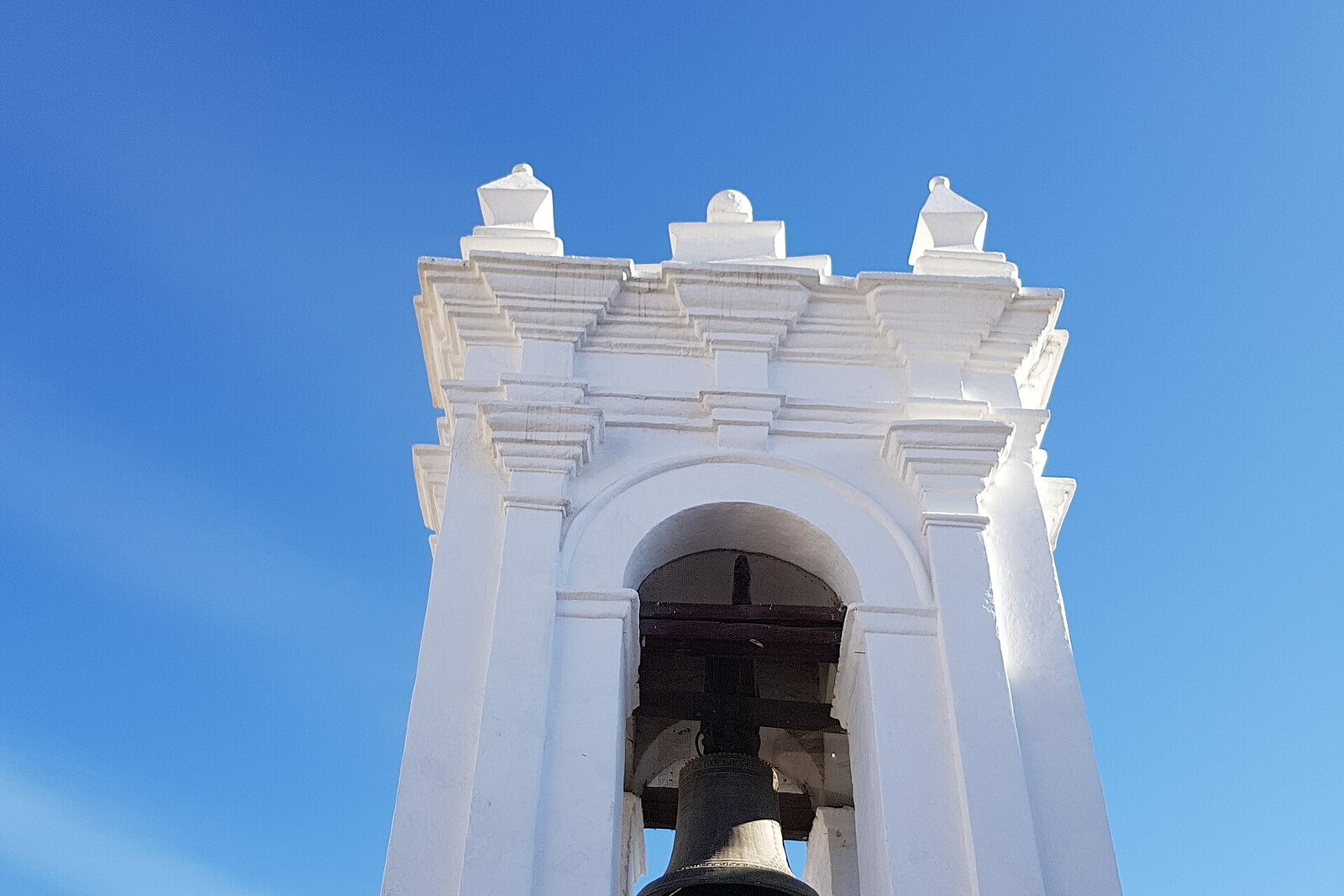 A bell in the white stepped tower of Saint Francis against a blue sky.