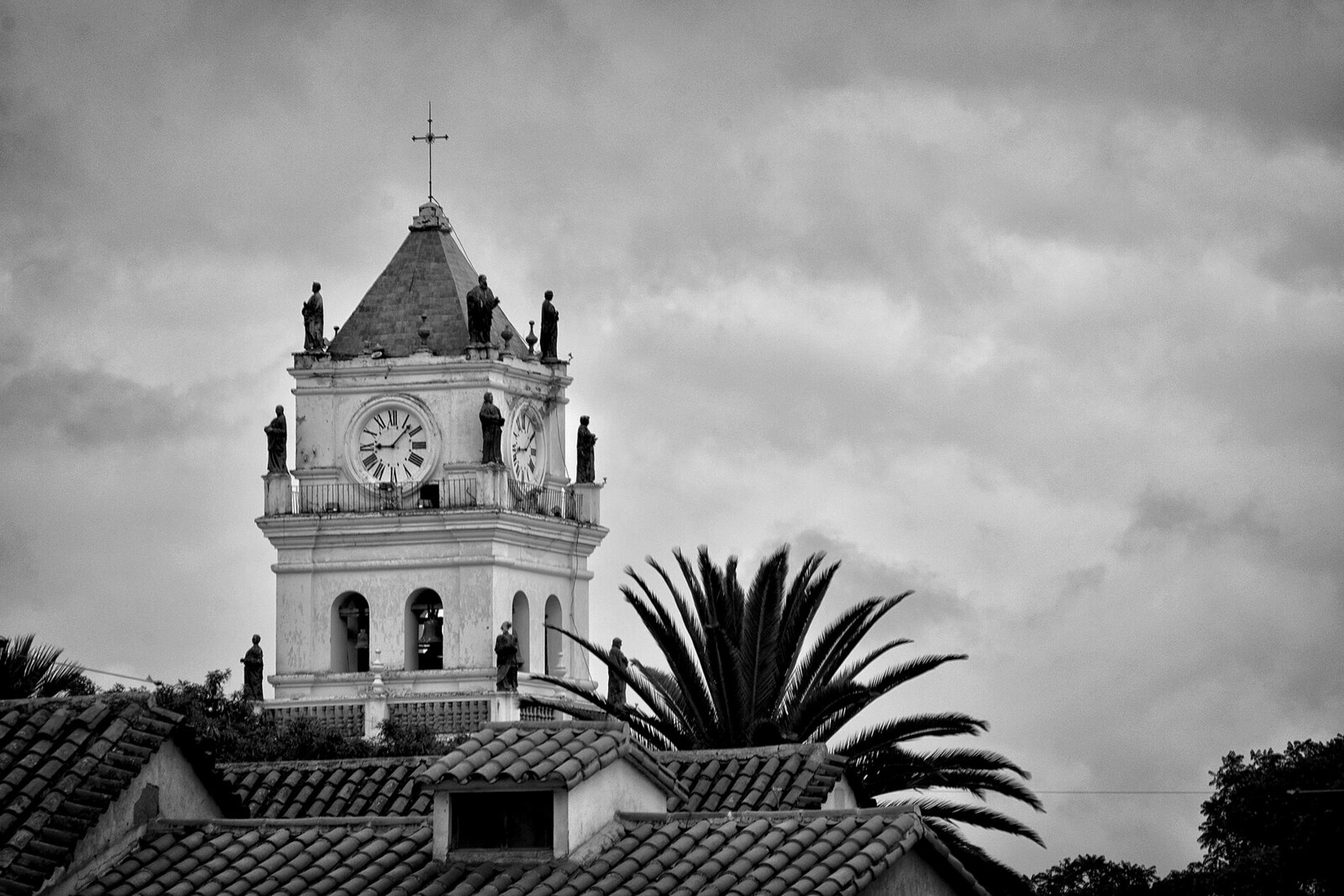 The black-and-white clock tower of Sucre Cathedral above tiled roofs.
