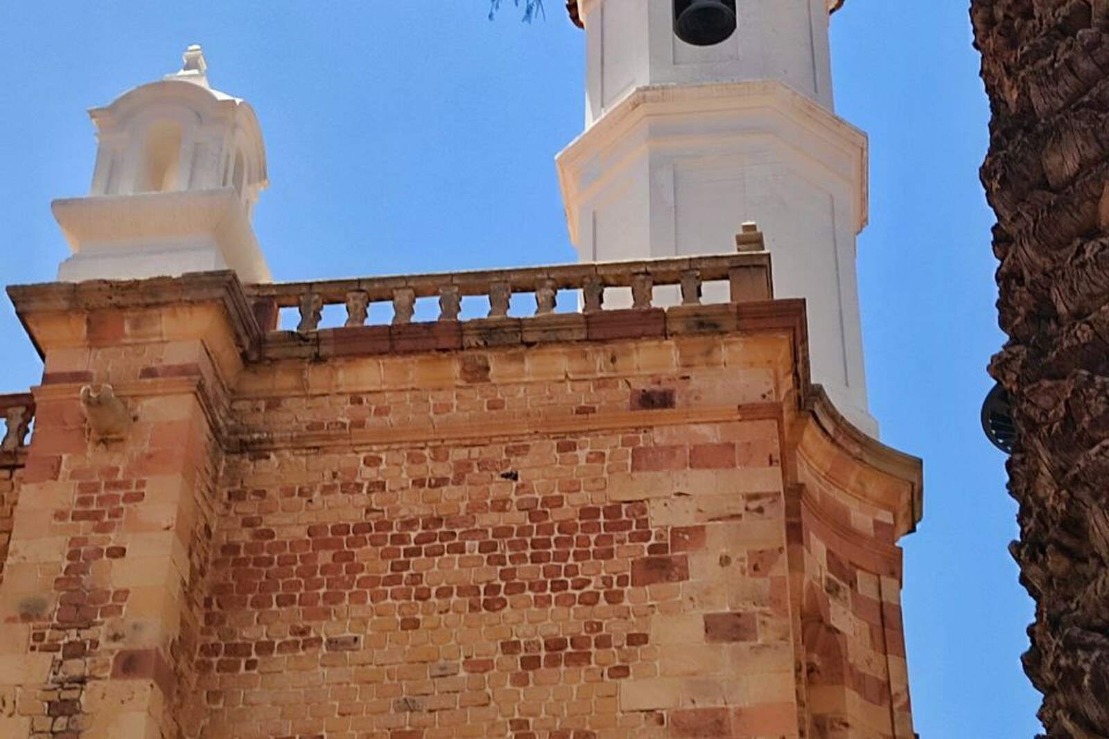 A red stone wall and the white bell tower of San Felipe Neri.