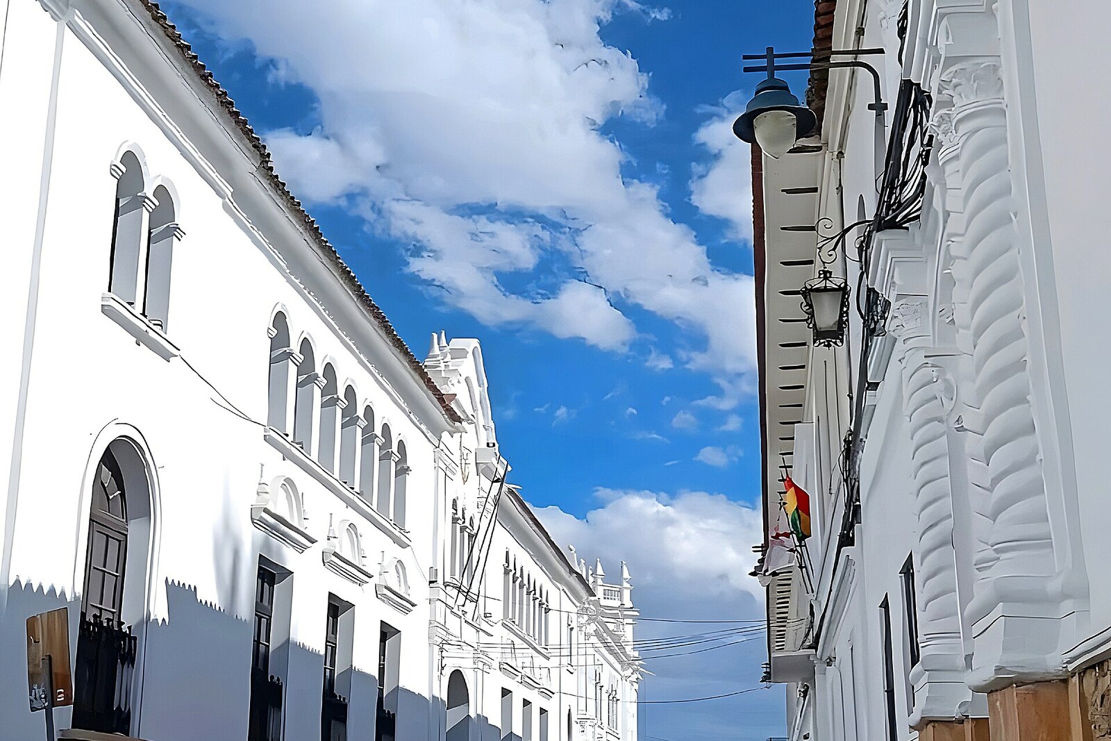 Rue de Sucre avec des façades blanches, des soubassements en pierre et des tuiles rouges.