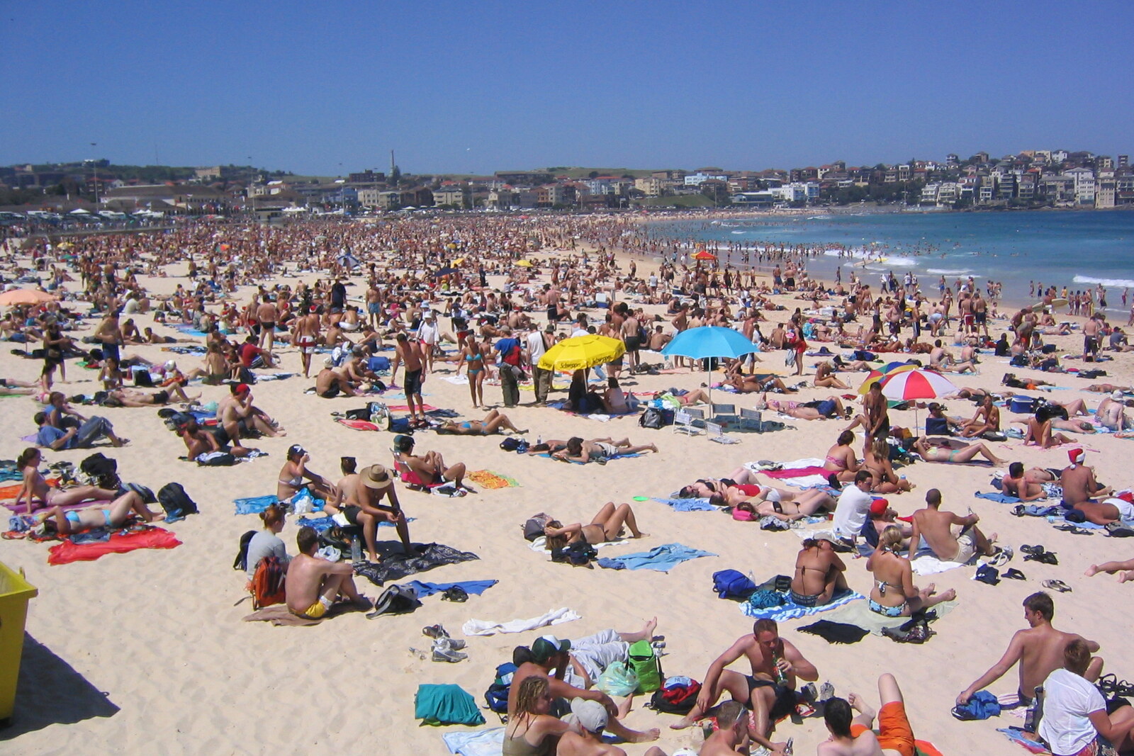 Bondi Beach with white sand, surfers, and blue water beneath a clear sky