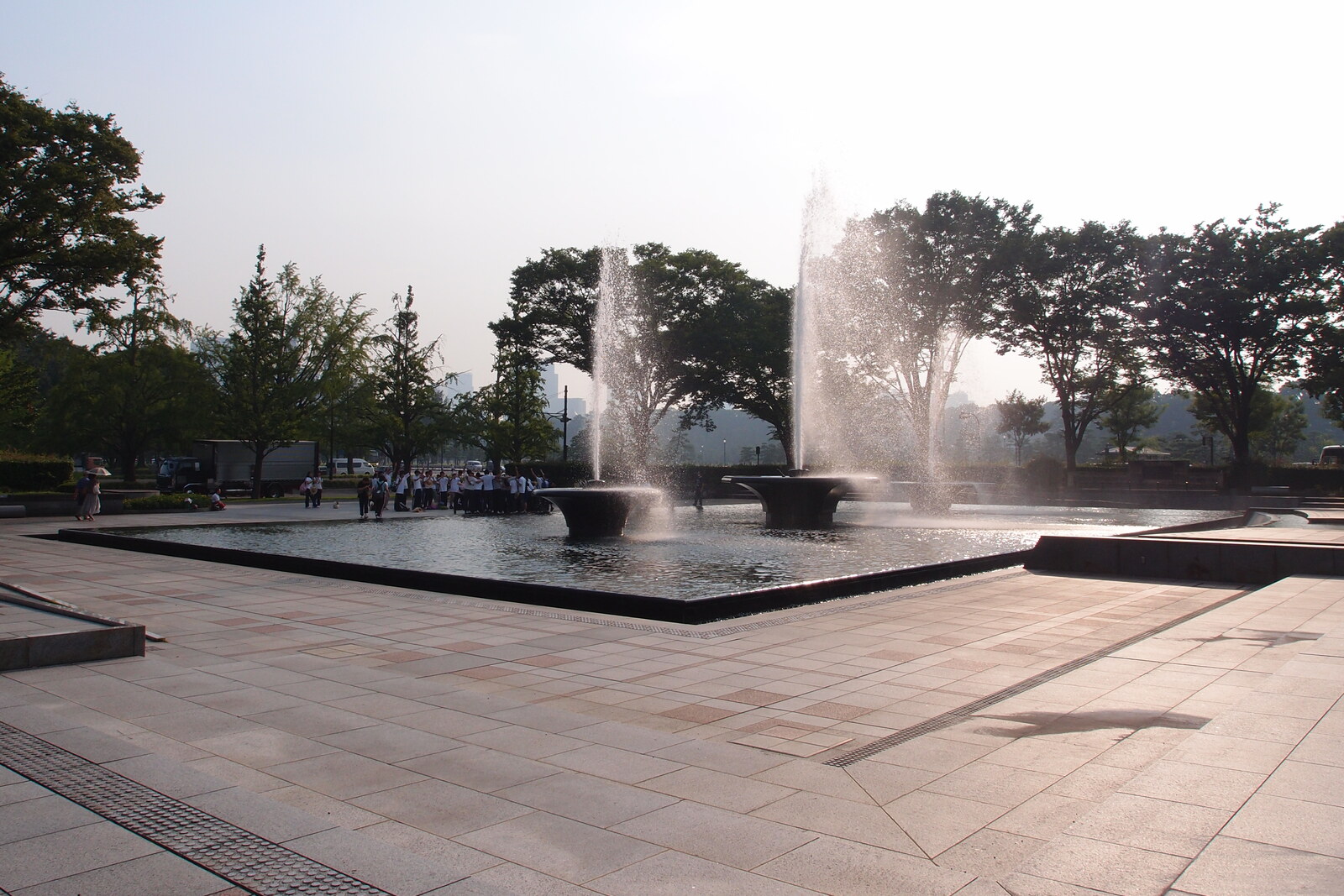 Tall fountain jets in an open plaza surrounded by trees