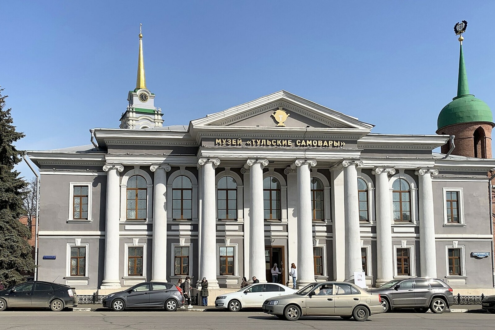 The gray colonnaded facade of the Tula Samovar Museum; the Kremlin's red-brick tower is visible on the right.