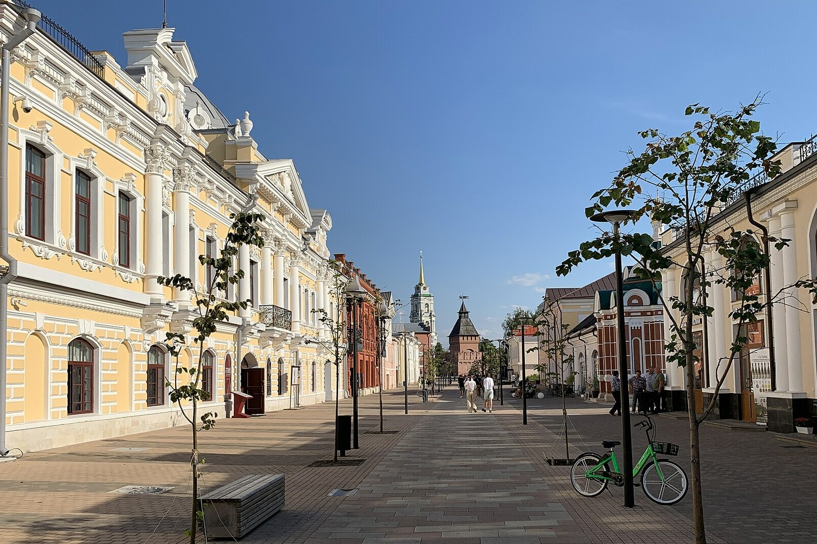 Pedestrian Metallistov Street with yellow-and-white merchants' facades and a Kremlin tower in the distance.