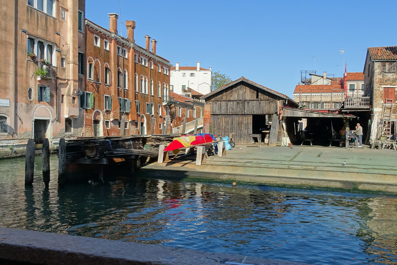 Wooden workshops of the San Trovaso boatyard, with a gondola hauled out of the water, against the backdrop of the canal.