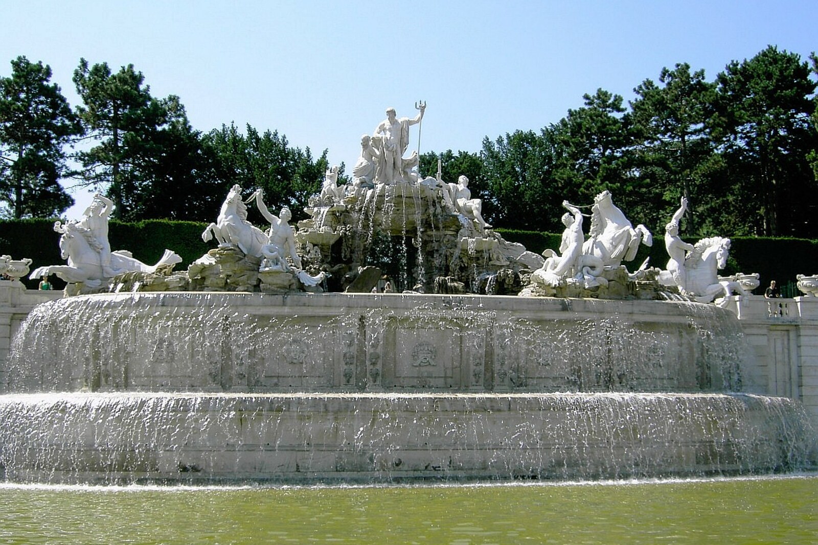 Fuente de mármol blanco con figuras de Neptuno y tritones ante una colina verde