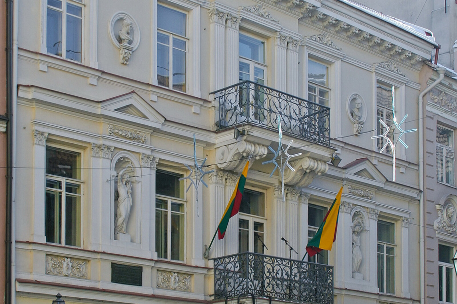 The light-colored façade of the House of the Signatories, with two balconies and flags.