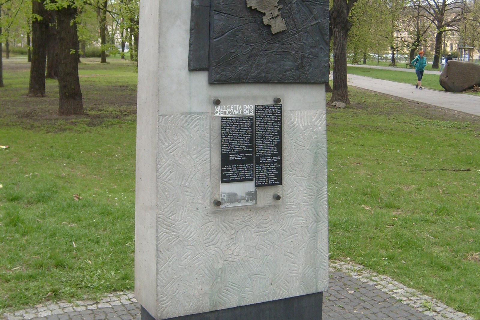 A granite strip and a memorial plaque on the sidewalk beside a green park.
