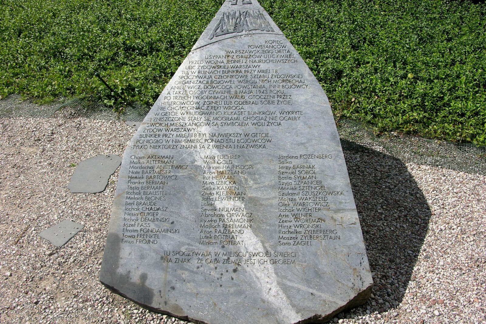 A granite obelisk on a grassy hill with trees around it.