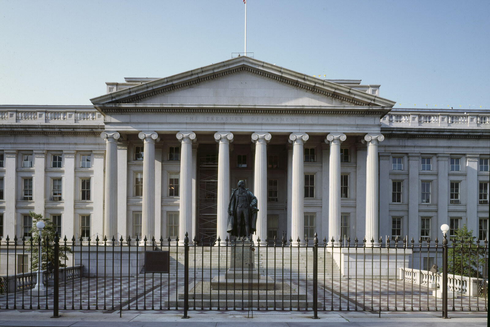 The long colonnade of the Treasury Building with a bronze statue of Alexander Hamilton in front of the entrance.