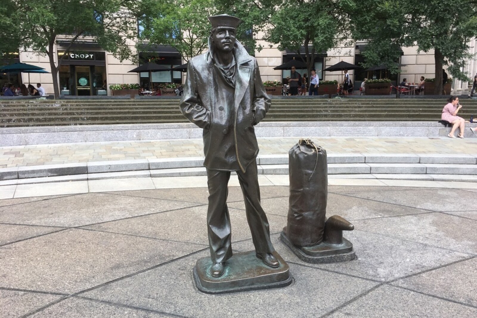 A bronze sailor stands on a pedestal in a granite plaza featuring a map of the world.