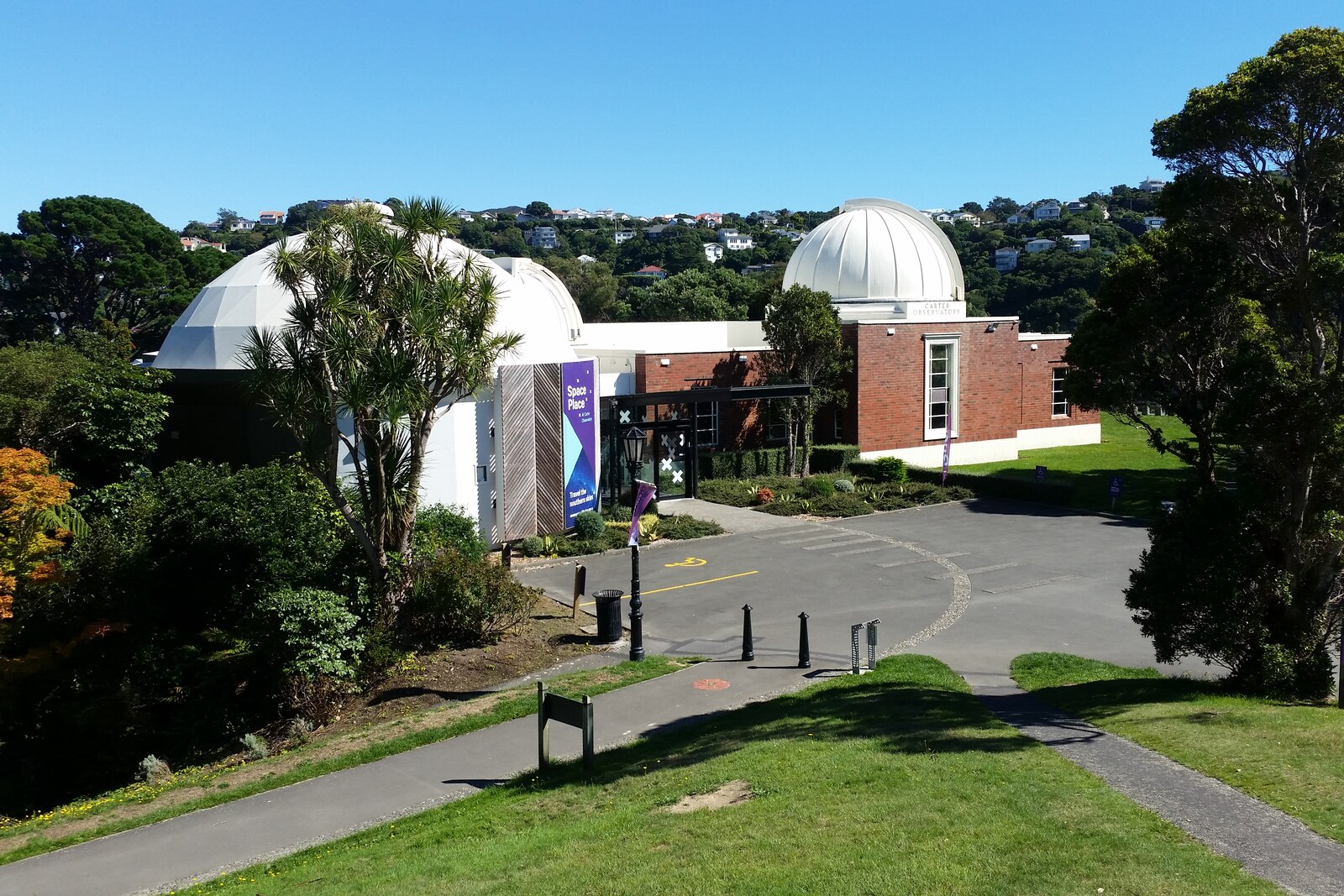 A white observatory building with a planetarium sphere and green trees around it.